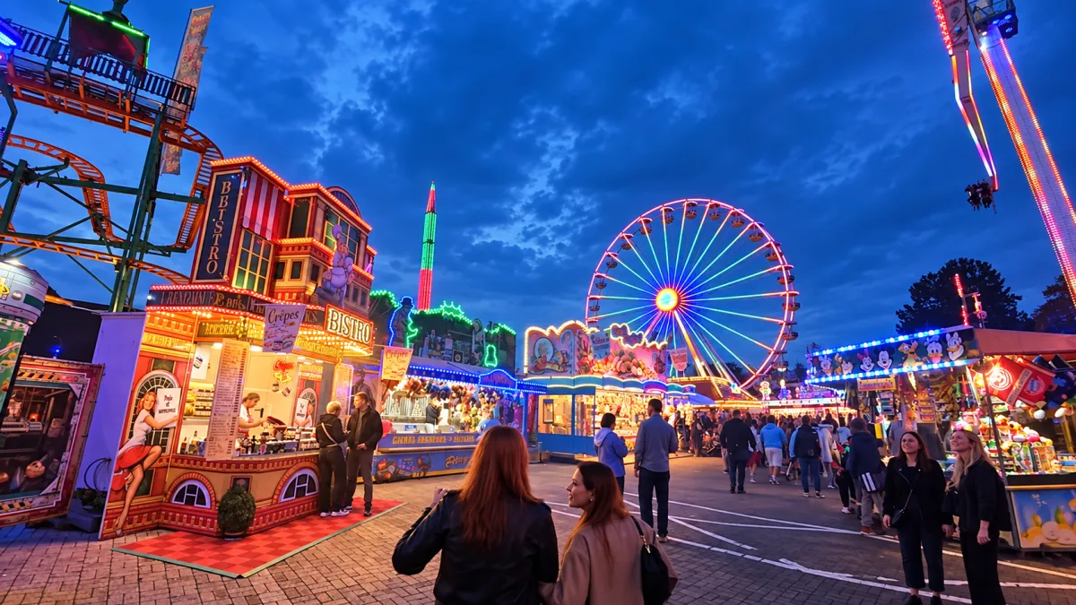 Beleuchteter Jahrmarkt am Abend mit Riesenrad, Fahrgeschäften, Kirmesbuden und Besuchern auf dem Festgelände